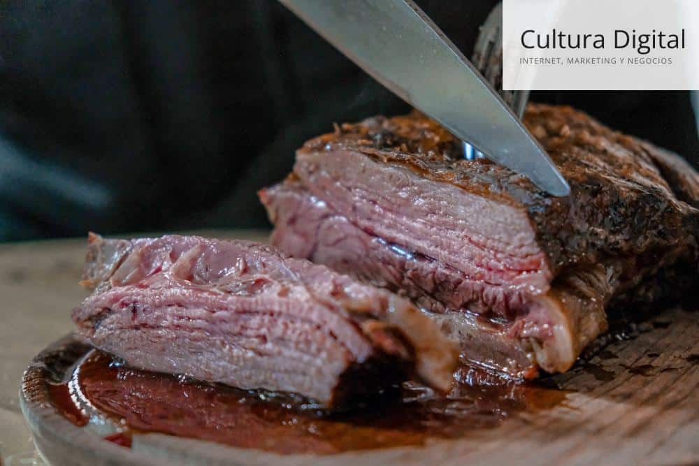 person slicing juicy medium rare meat on top of brown wooden cutting board